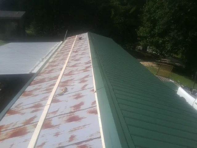 Old rusted panels beside newly installed green metal roofing — Wind Damage Roof Repair by Roofing Brothers in Belmont